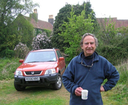 John Crook standing in front of his car, with a mug in his hand 